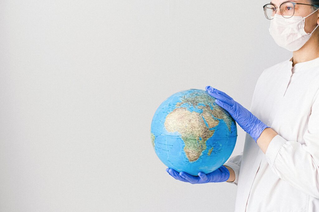 Person in mask and gloves holding a globe, symbolizing global healthcare during pandemic.